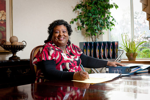 A woman smiles while writing at her desk in a professional office setting.