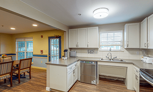 A modern kitchen with white cabinets, a stainless steel dishwasher, and a large window.