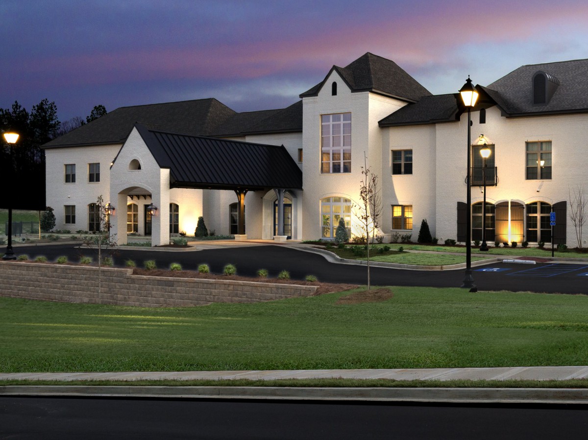 A luxurious mansion illuminated in the evening with a well-manicured lawn.