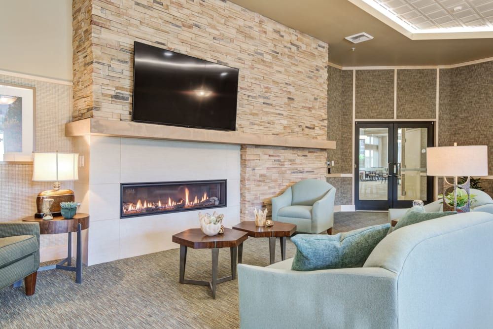 A modern living room featuring a stone fireplace with a wall-mounted television above, complemented by comfortable armchairs and a coffee table.