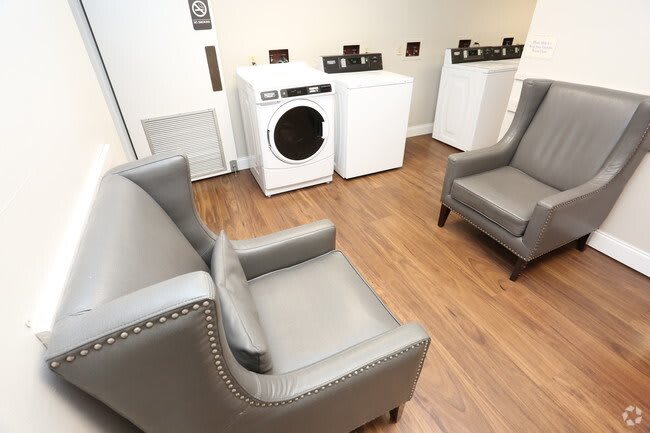 A laundry room featuring a washer and dryer alongside comfortable armchairs and a wooden floor.