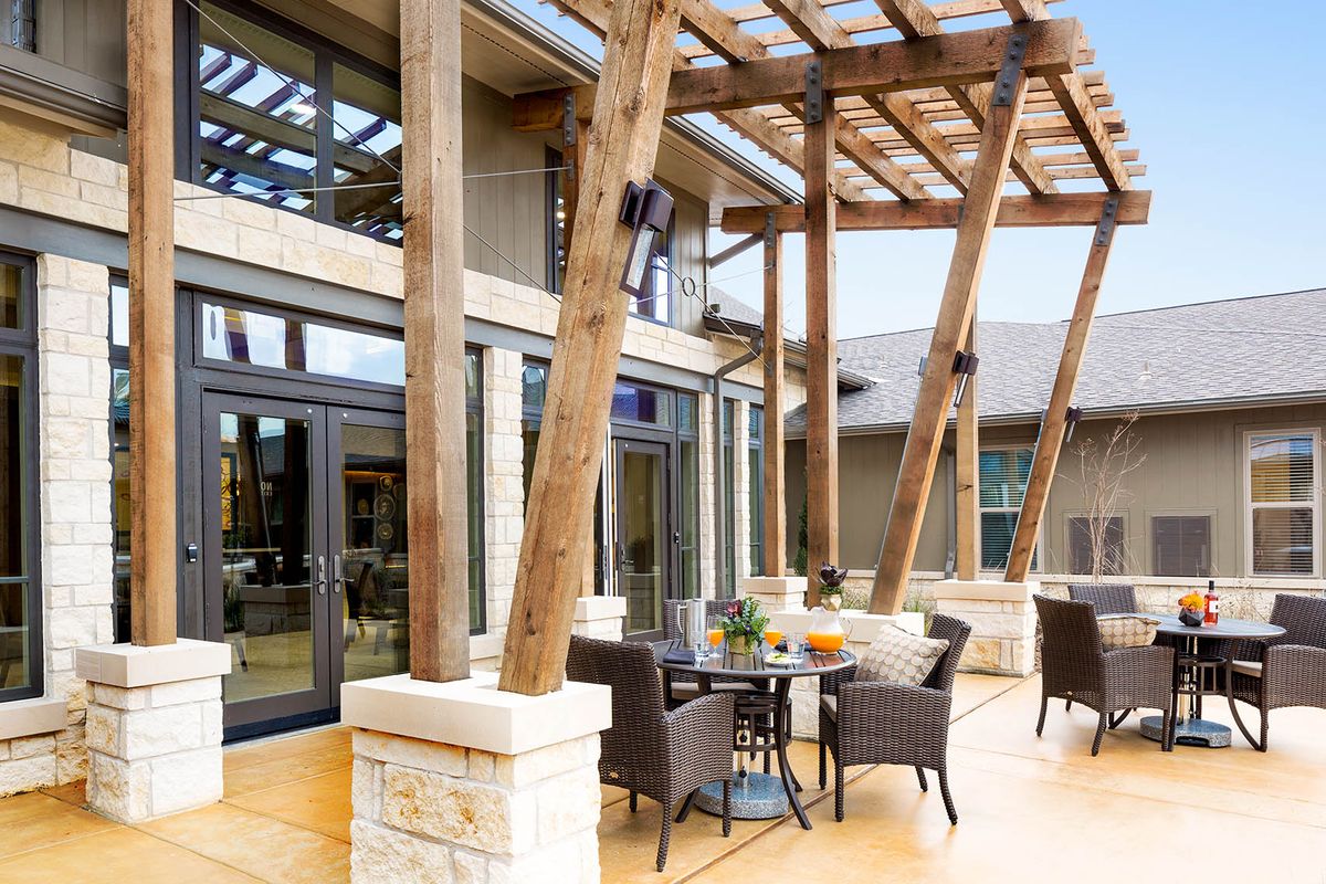 A modern outdoor patio with a wooden beam pergola and wicker furniture set on a spacious deck.
