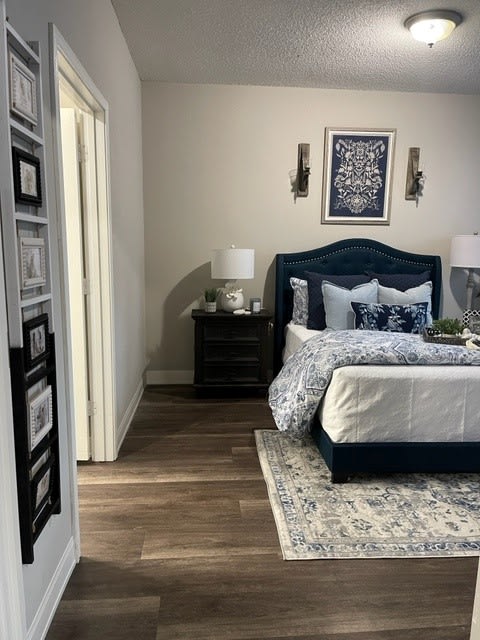 A well-decorated bedroom featuring a dark blue bed with patterned bedding, flanked by two bedside tables and lamps, complemented by artwork on the wall and a rug.