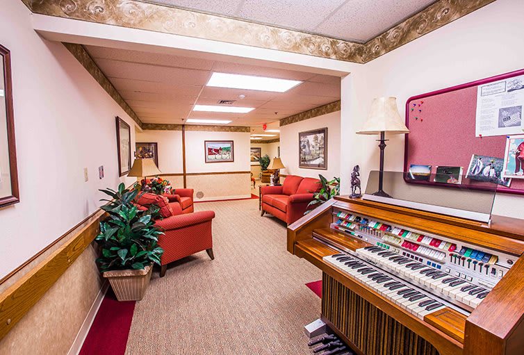 A cozy lounge area featuring red couches, an organ, and decorative plants.