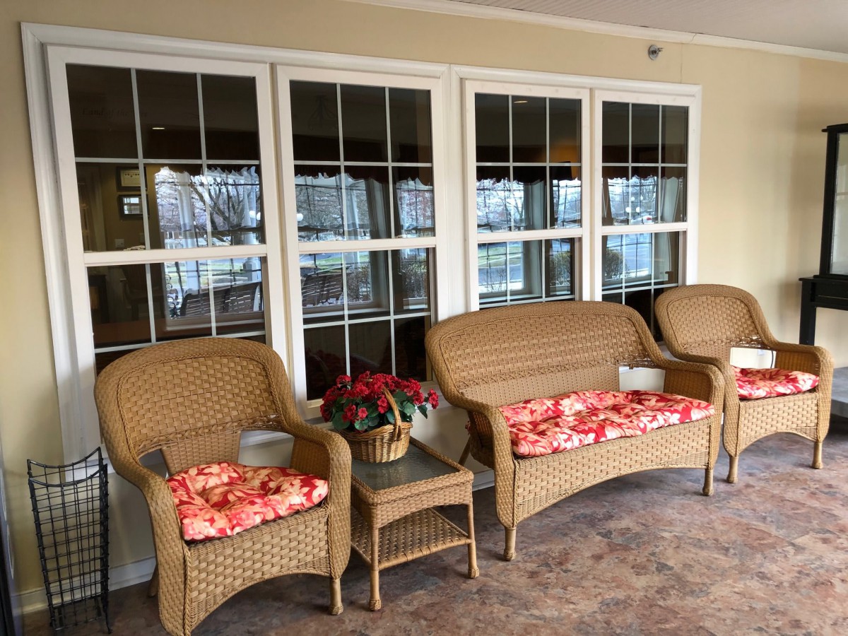 A cozy patio with wicker furniture and floral cushions, overlooking large windows.