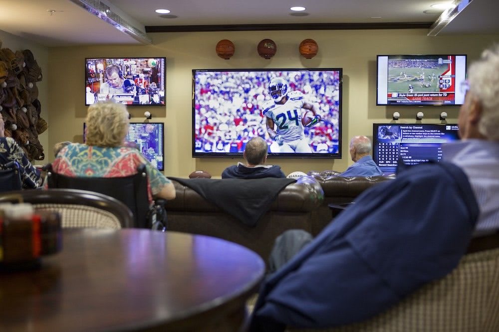 Group of people watching a football game on multiple TVs in a lounge.