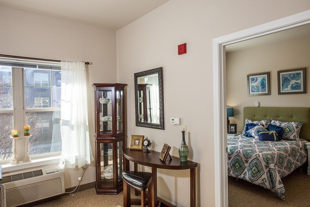 A cozy interior featuring a small desk, mirror, and a glimpse into a bedroom.