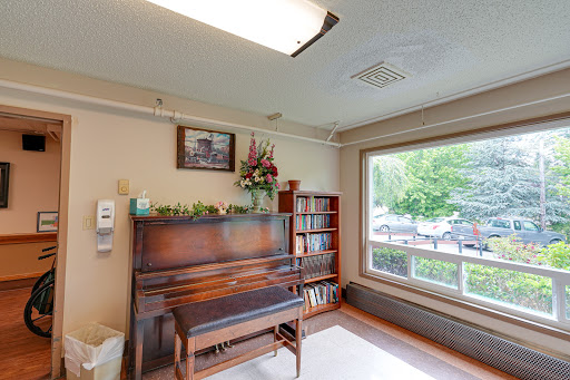 A cozy corner featuring a wooden piano, a bookshelf filled with books, and a window that allows natural light to flow in.