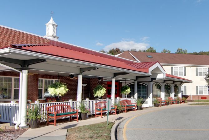The entrance of a building with a red roof, featuring benches and hanging plants.
