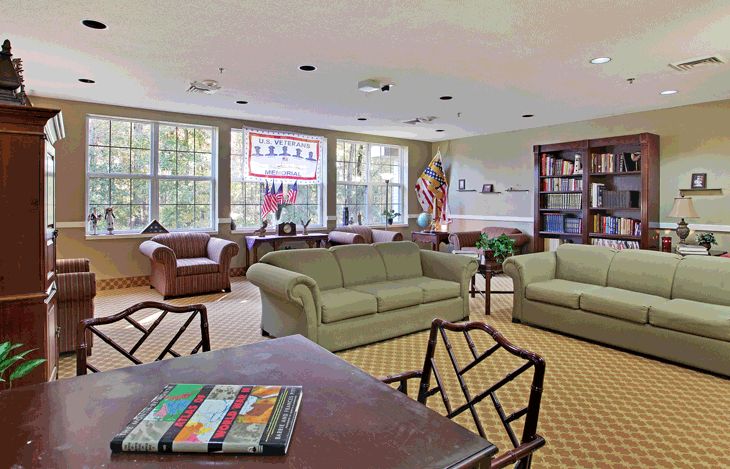A spacious living room with comfortable seating, large windows, and a bookshelf.