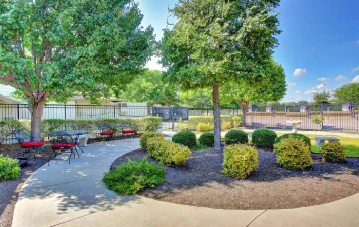 A peaceful garden with a pathway and outdoor seating surrounded by trees and bushes.