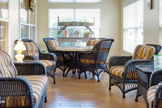 A cozy dining area with wicker furniture and striped cushions, illuminated by natural light from large windows.