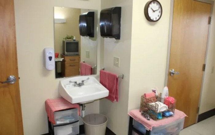 A small medical room with a sink, mirror, and clock on the wall.
