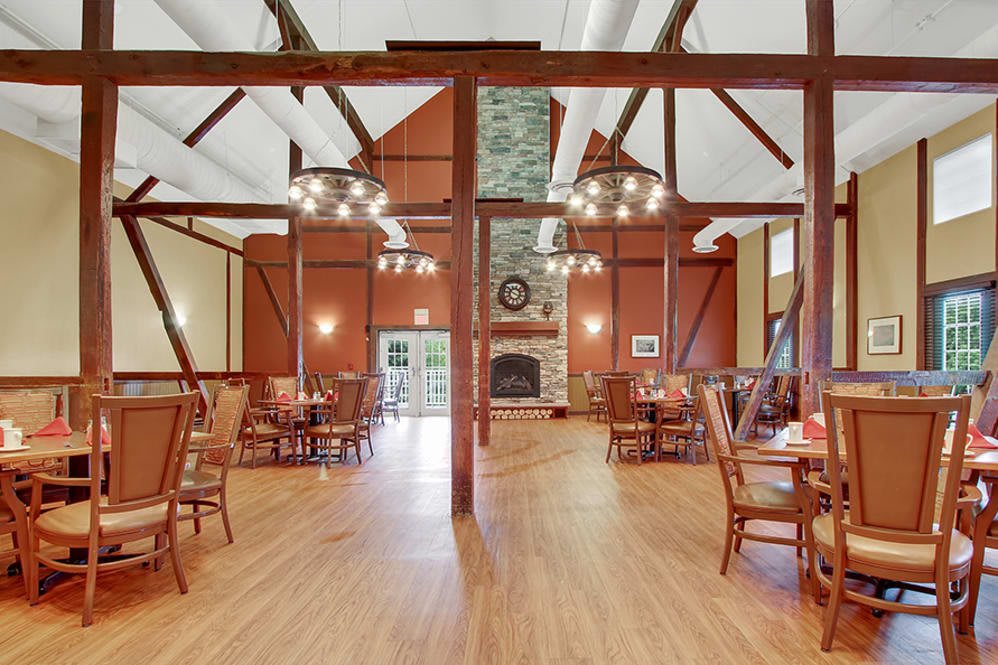 A spacious dining room with rustic wooden beams, chandeliers, and a central fireplace.