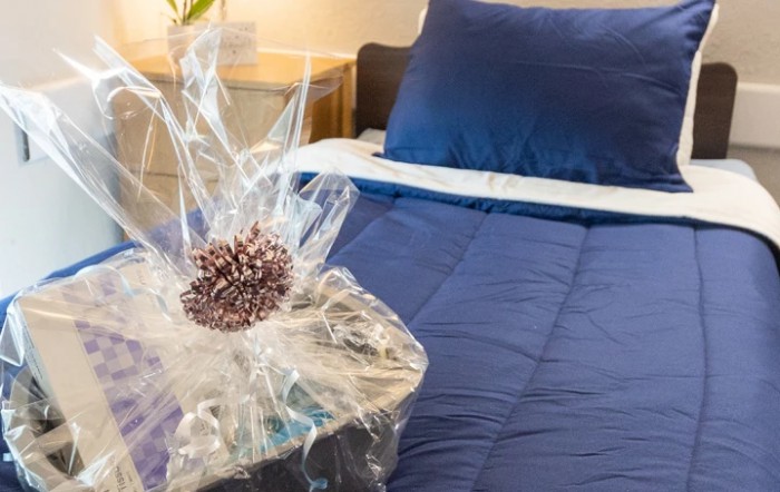 A neatly made bed with blue bedding and a decorative wrapped gift placed nearby.