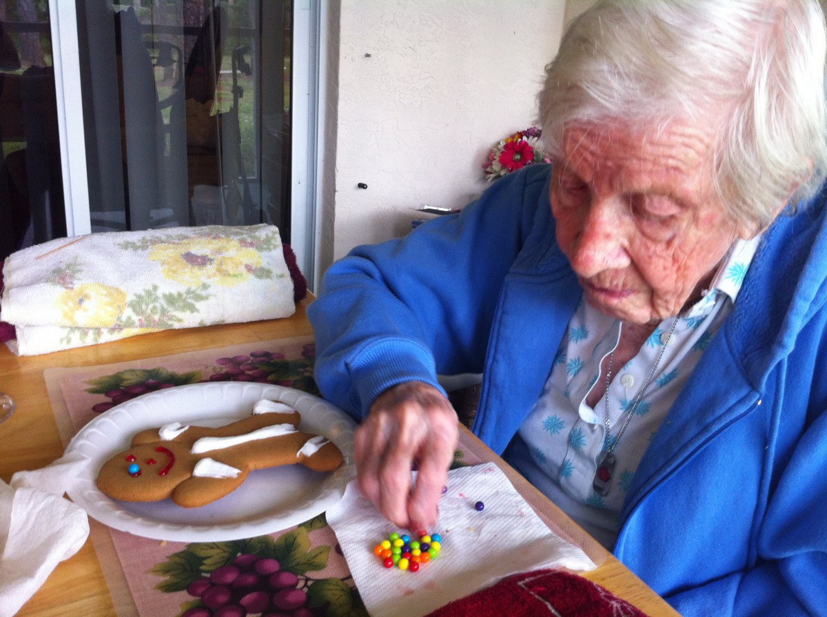 An elderly person sits at a table decorating gingerbread cookies with colorful candies.