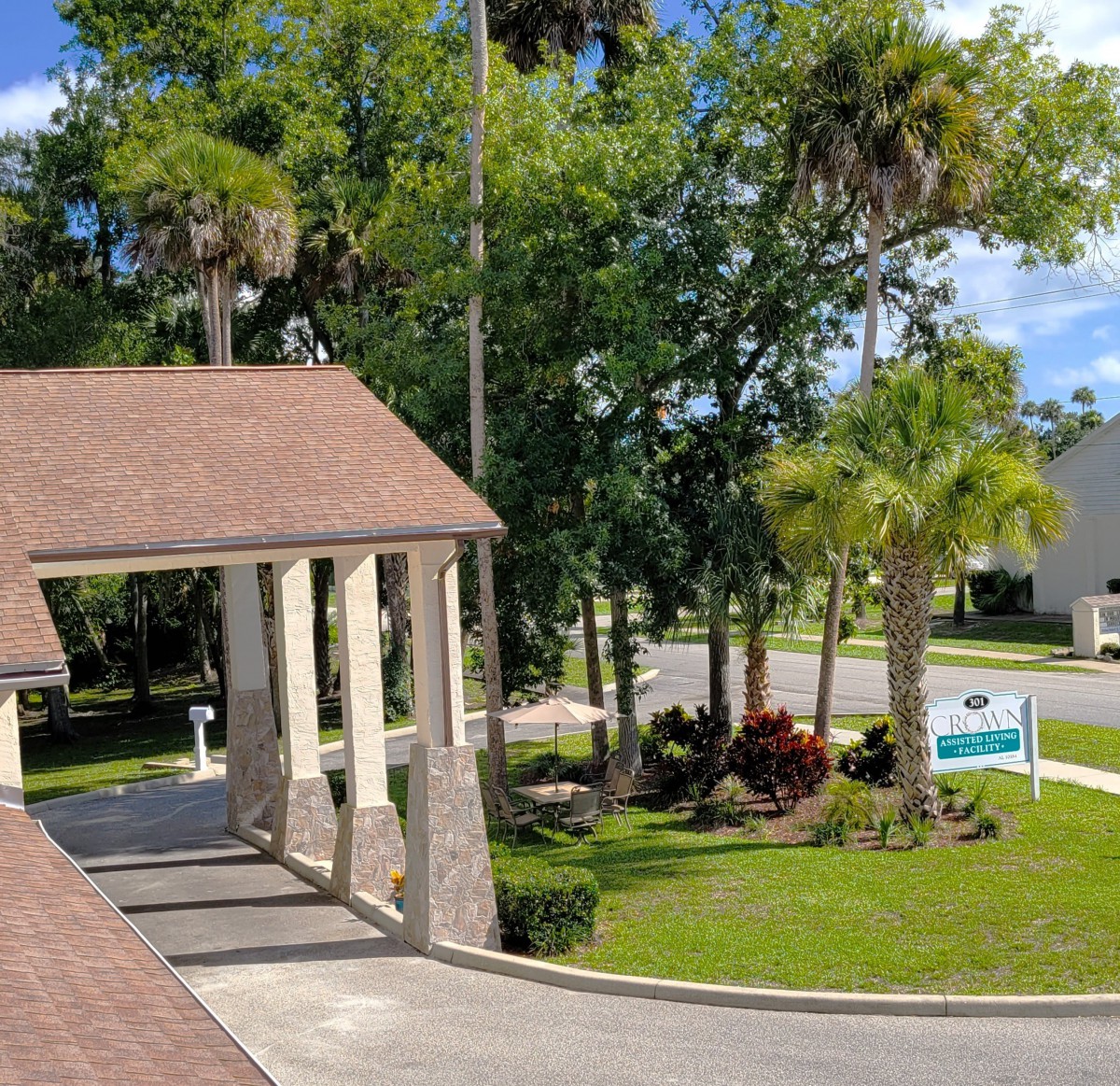A view of a building with a covered driveway, surrounded by lush greenery and palm trees.