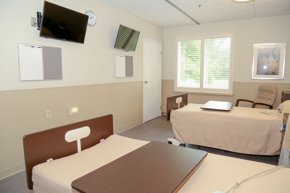 A clean and modern hospital room with two beds and wall-mounted televisions.