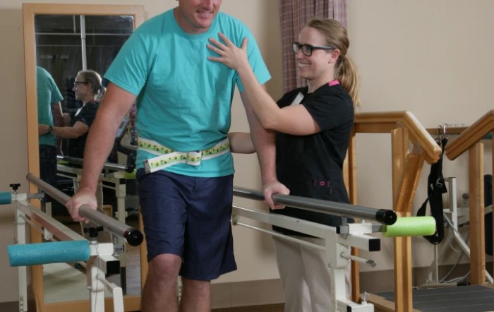 A healthcare professional assists a patient during physical therapy with a walking aid.