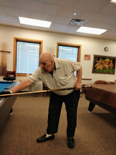 An elderly man focused on making a shot at the billiard table.