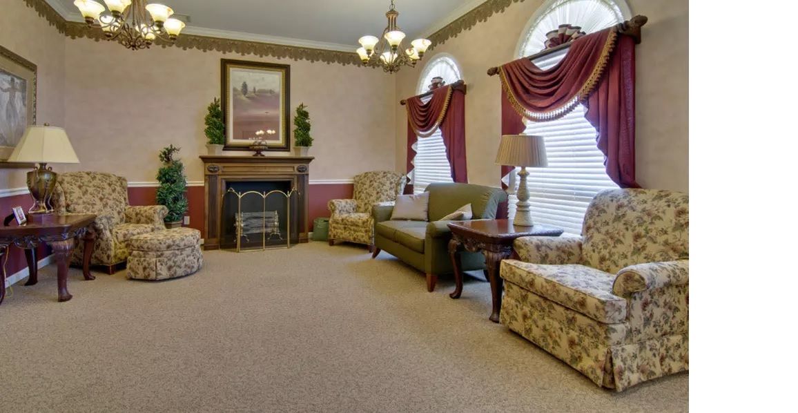 A traditional living room with elegant furnishings, featuring a fireplace and large windows with draped curtains.