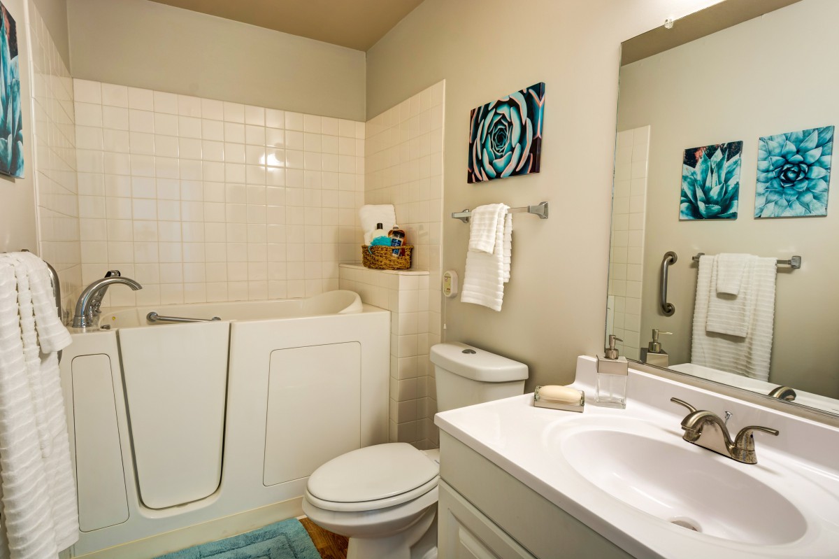 A modern bathroom featuring a walk-in tub, sink, and toilet with tasteful decor.