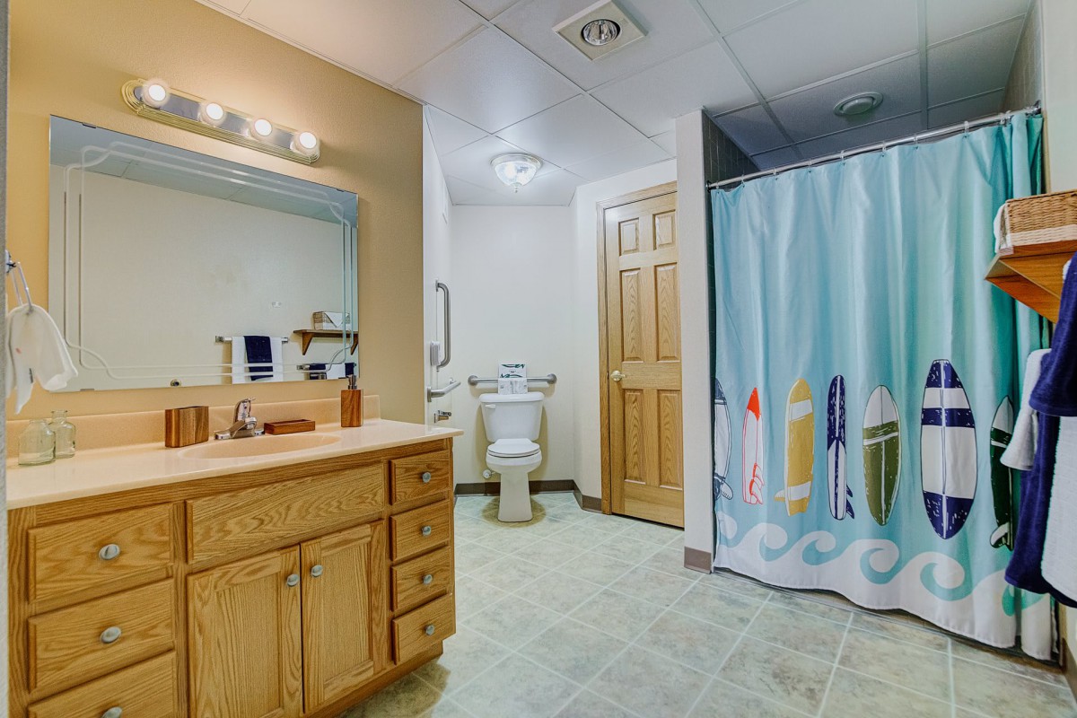 A well-lit bathroom featuring a wooden vanity, mirror, toilet, and a colorful shower curtain.