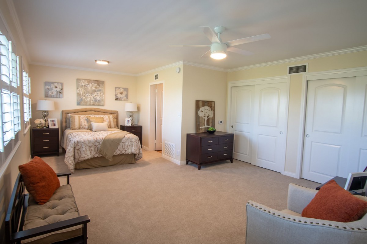 A spacious and elegantly decorated bedroom with neutral tones, featuring a large bed, dresser, and ceiling fan.