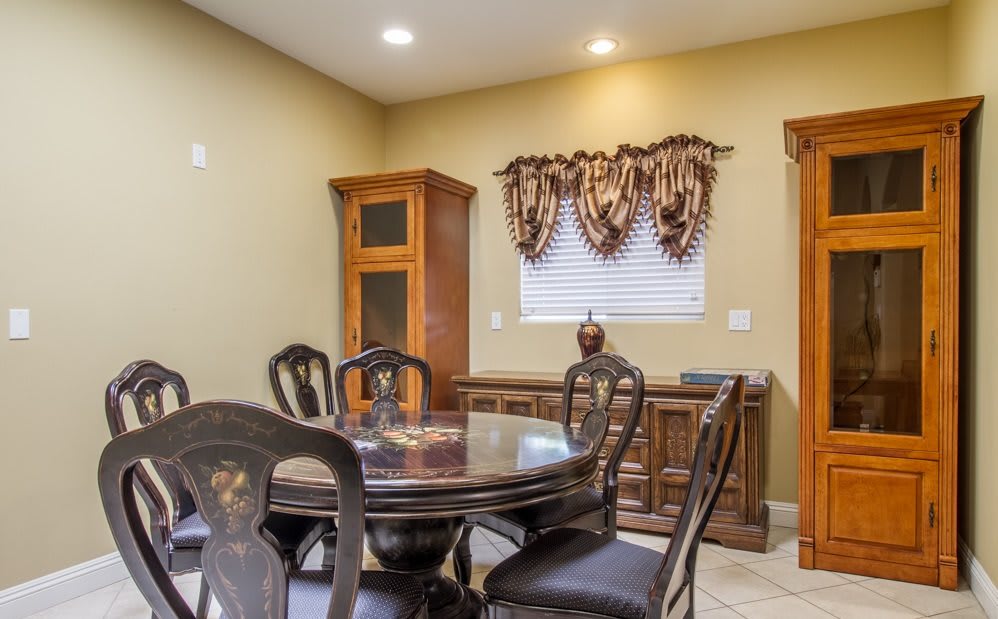 A traditional dining room featuring a wooden table and chairs, a cabinet, and decorative window treatments.