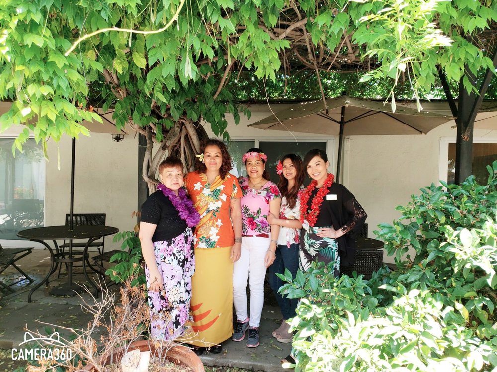 A group of people smiling and standing together outdoors, surrounded by lush greenery.