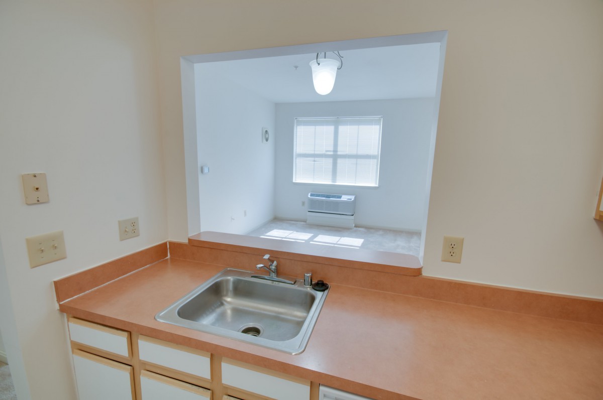 A view from the kitchen through an open space, featuring a sink and countertop.