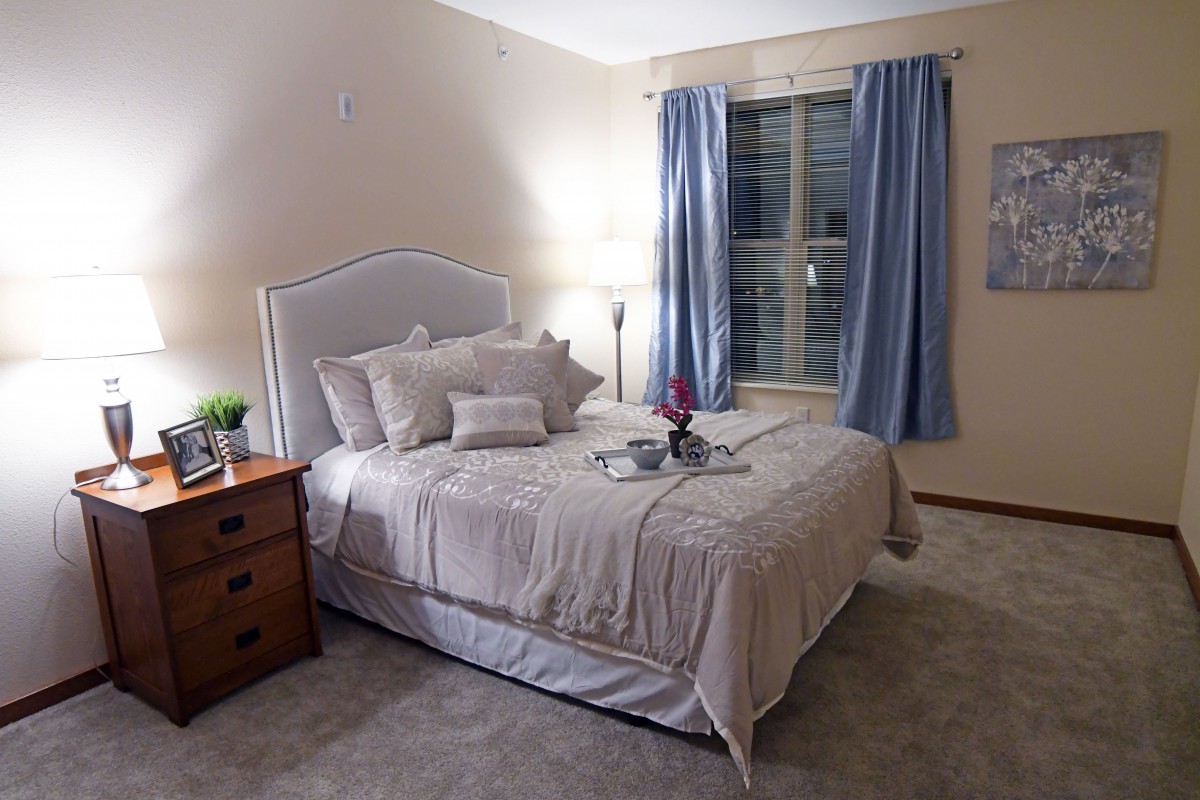 A cozy bedroom featuring a neatly made bed with multiple pillows and a nightstand with a lamp.