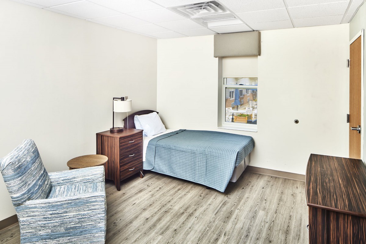 A minimalist bedroom with a single bed, wooden nightstand, and a window.