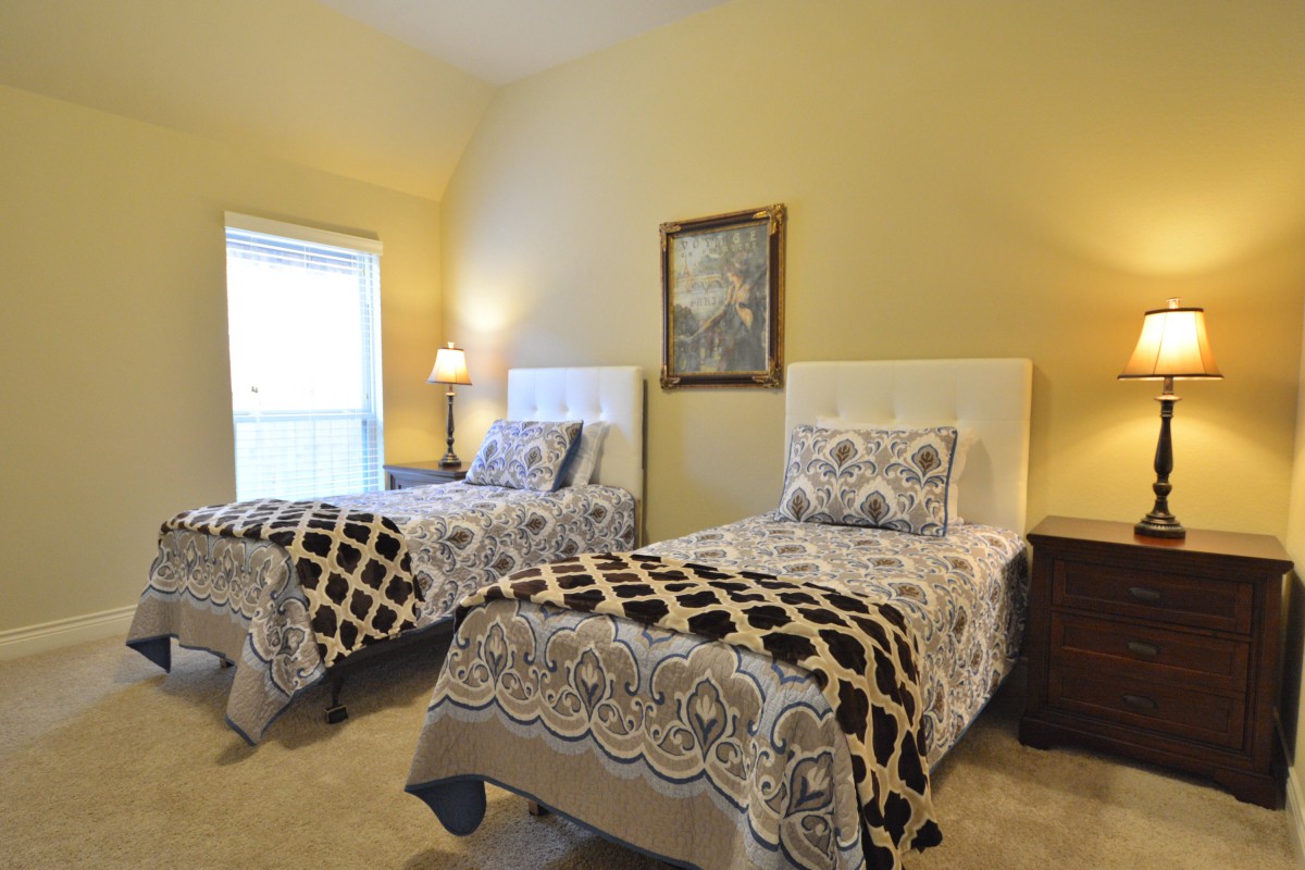 A cozy bedroom featuring two twin beds with patterned bedding, a bedside lamp, and wall art.