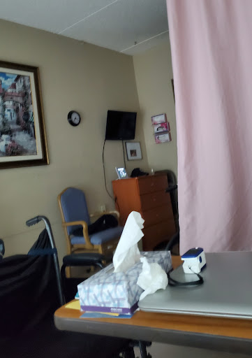 A view of a hospital patient room featuring a curtain for privacy, a chair, and some tissues on a table.
