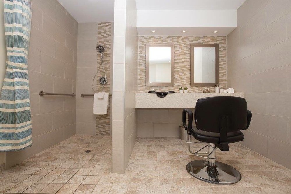 A modern accessible bathroom with a vanity area, mirrors, and a tiled shower space.
