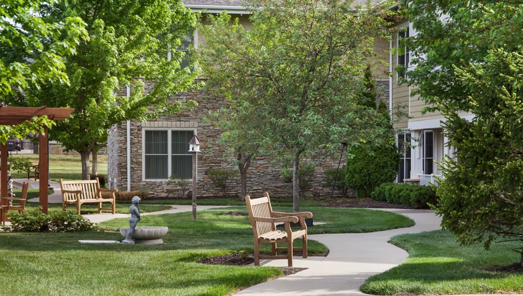 A peaceful garden area with a bench and walkway surrounded by trees and grass.