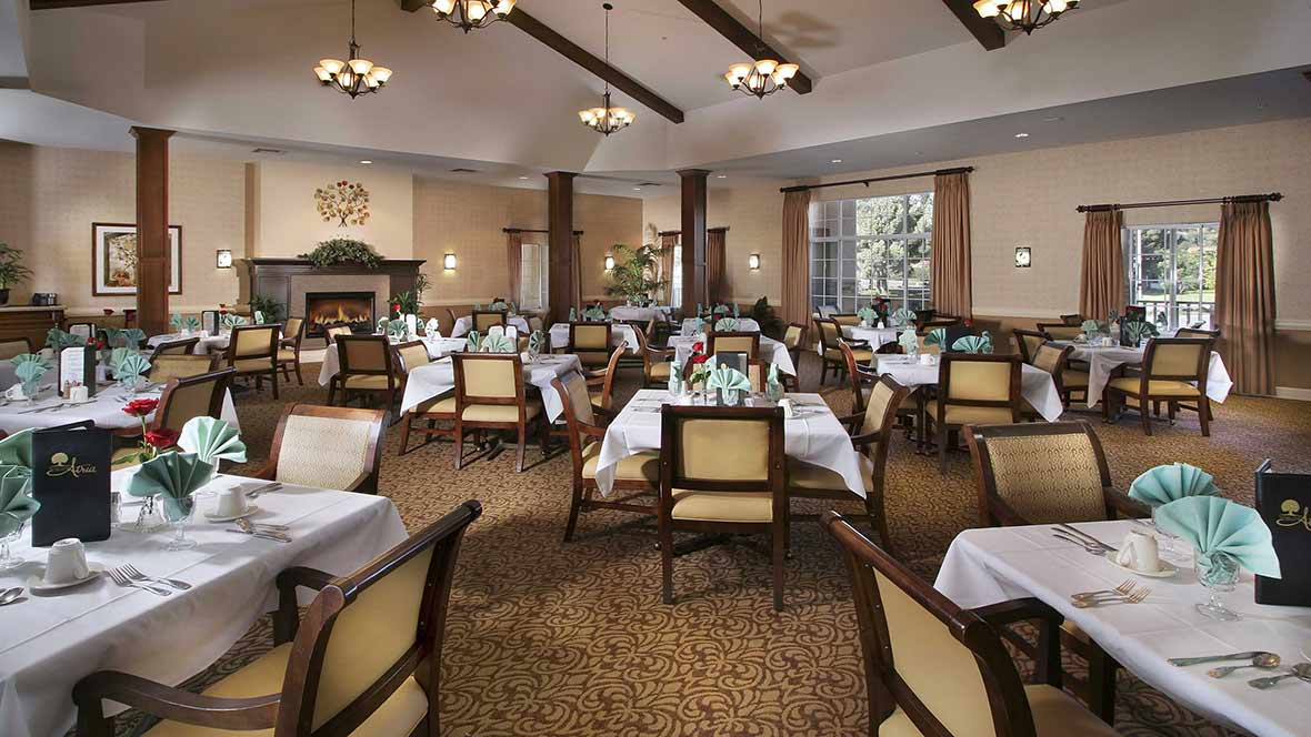 An elegantly decorated dining room with neatly arranged tables and chairs, adorned with chandeliers.