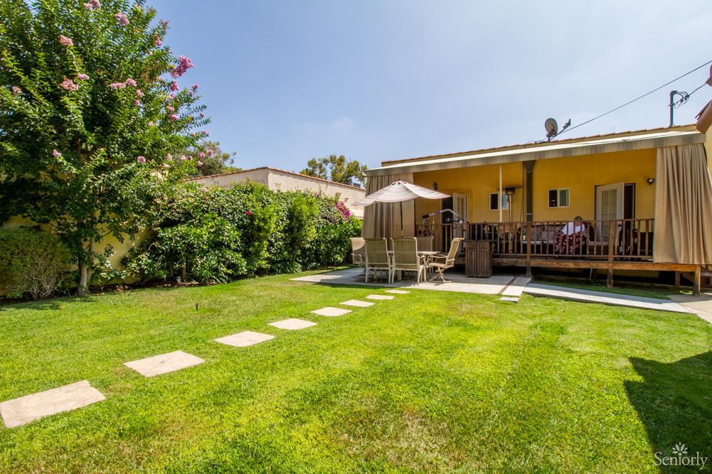 A charming backyard featuring a spacious lawn, patio with outdoor seating, and lush greenery.