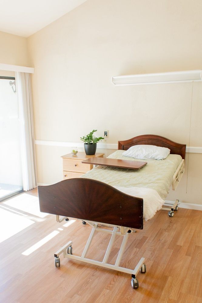 A clean and organized hospital room with a single bed and a small drawer beside it.
