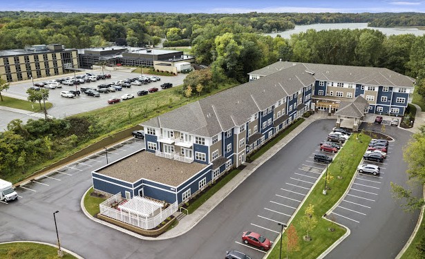 Aerial view of a large residential building with an adjacent parking lot and surrounding greenery.