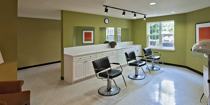 A modern hair salon interior with stylish barber chairs and mirrors against green walls.