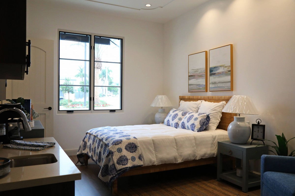 A cozy bedroom featuring a neatly made bed with patterned bedding, two pieces of artwork on the wall, and natural light streaming through the windows.