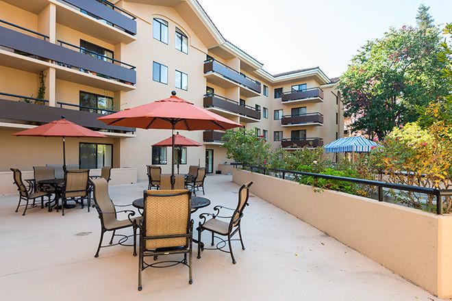 An outdoor patio area with tables, chairs, and umbrellas in a residential apartment complex.