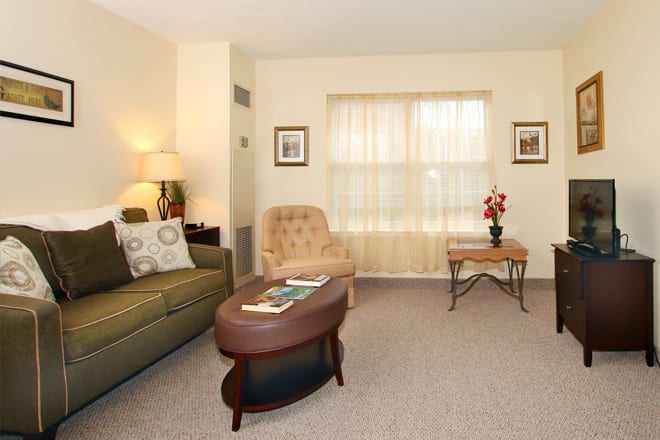 A cozy living room with a sofa, armchair, and coffee table in front of a curtained window.