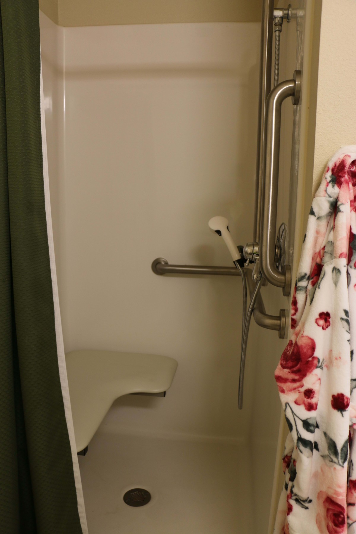 An accessible shower with grab bars and a built-in seat, featuring a floral curtain.