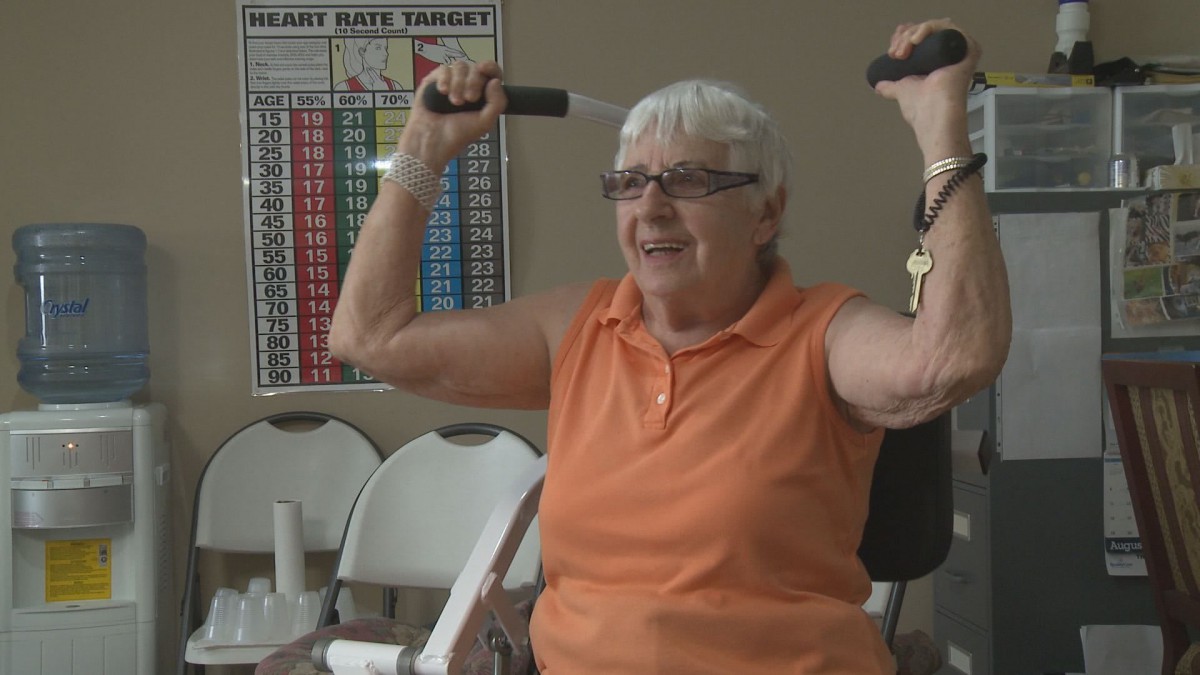 A senior woman smiling while lifting dumbbells in an exercise class.