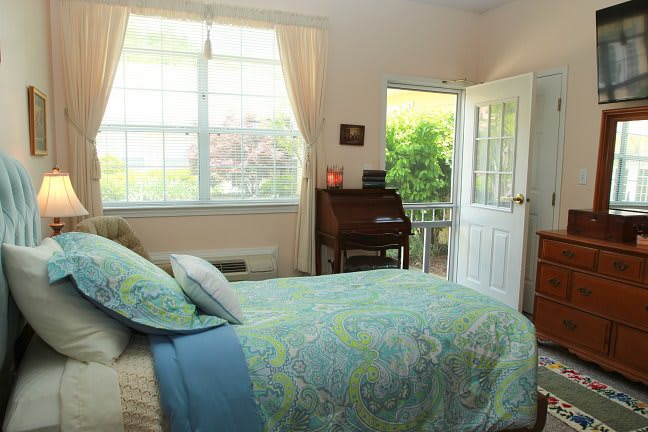 A cozy bedroom with a bed, desk, and open door leading to a garden.