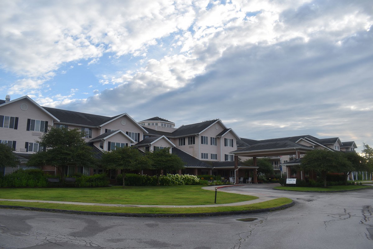 A residential building surrounded by greenery under a cloudy sky.