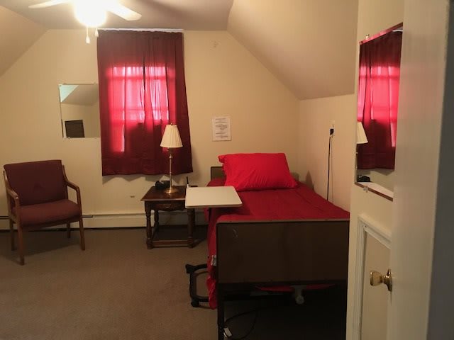 A small, neatly arranged bedroom with a bed, nightstand, and chair.